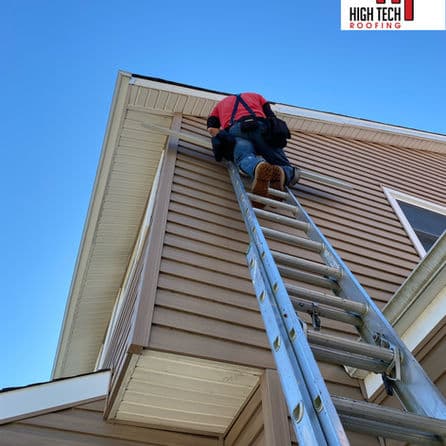 Roofer climbing ladder for home maintenance under clear blue sky. High Tech Roofing logo.