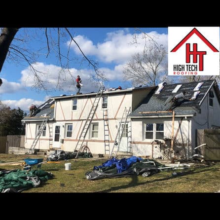 Workers installing a new roof on a house under a clear blue sky with ladders and tools.