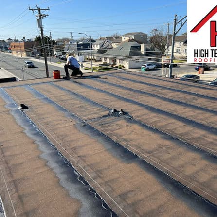 Worker applying roofing material on a flat commercial roof with urban landscape in background.