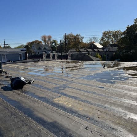 Flat roof with standing water and clear blue sky, overlooking residential buildings.