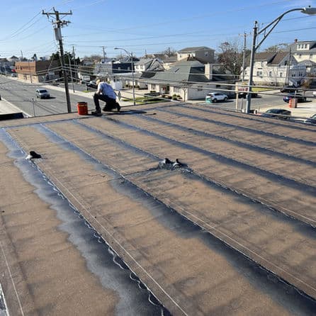 Worker repairing a flat roof on a commercial building in an urban neighborhood.