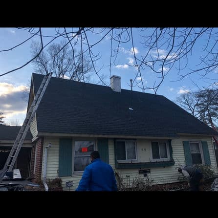 Workers inspecting a residential roof with a ladder under a blue sky and trees.