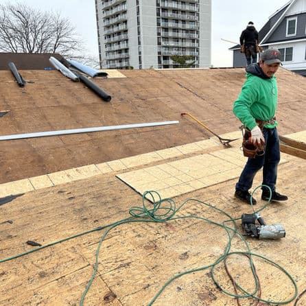 Roofer working on a sloped roof with tools and materials on an urban building site.