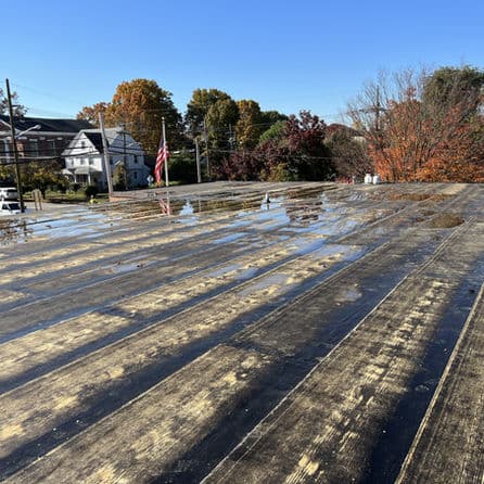 Flat commercial roof with water pooling, autumn trees and American flag in background.