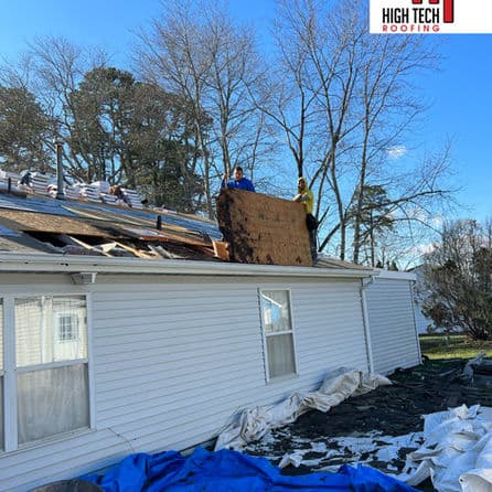 Roofing contractors replace shingles on a residential home under a clear blue sky.