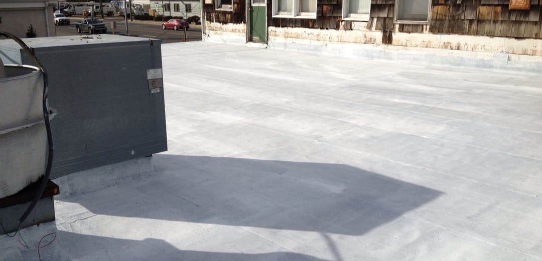 Flat commercial rooftop with HVAC unit and weathered building in background.