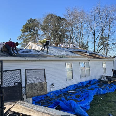 Workers applying a new roof on a house, with blue tarp covering the ground.