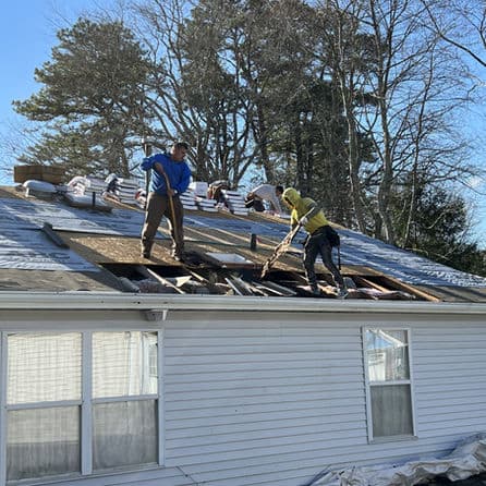 Workers replacing a roof, removing shingles and debris on a residential home.