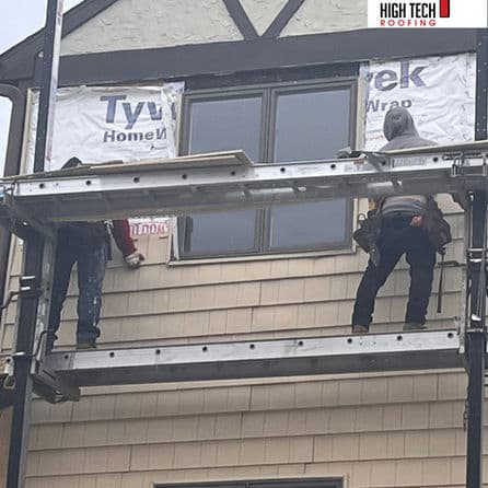 Workers installing Tyvek home wrap on a house during a roofing project, using scaffolding.